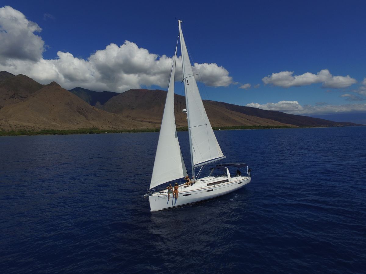 SV Kainani's mainsail and jib against trade-wind clouds