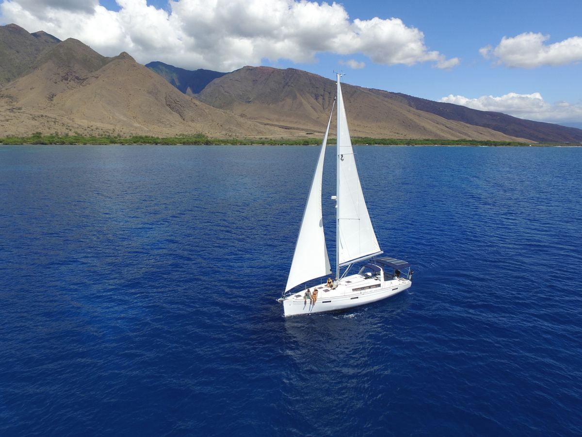 SV Kainani under sail beneath trade-wind clouds